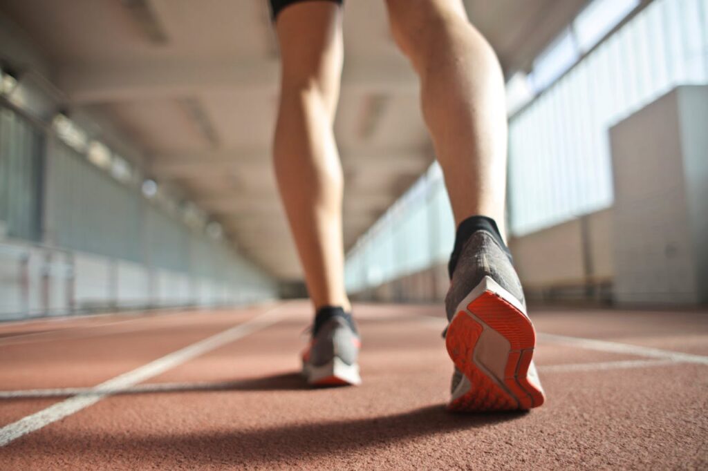 Back view of a runner's legs in a stadium, focusing on footwear and athletic motion.