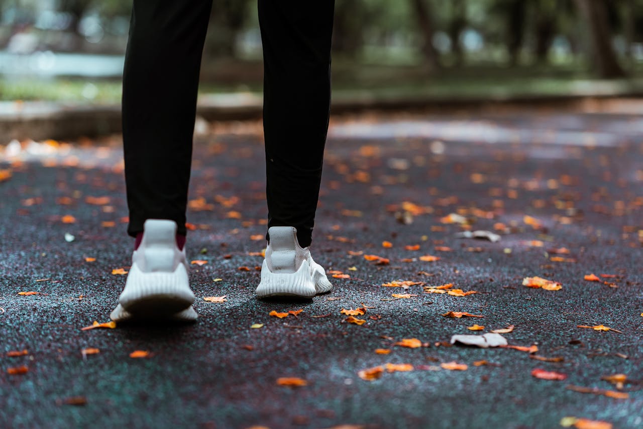 Person walking on a leaf-covered path in a park, wearing sneakers and leggings.